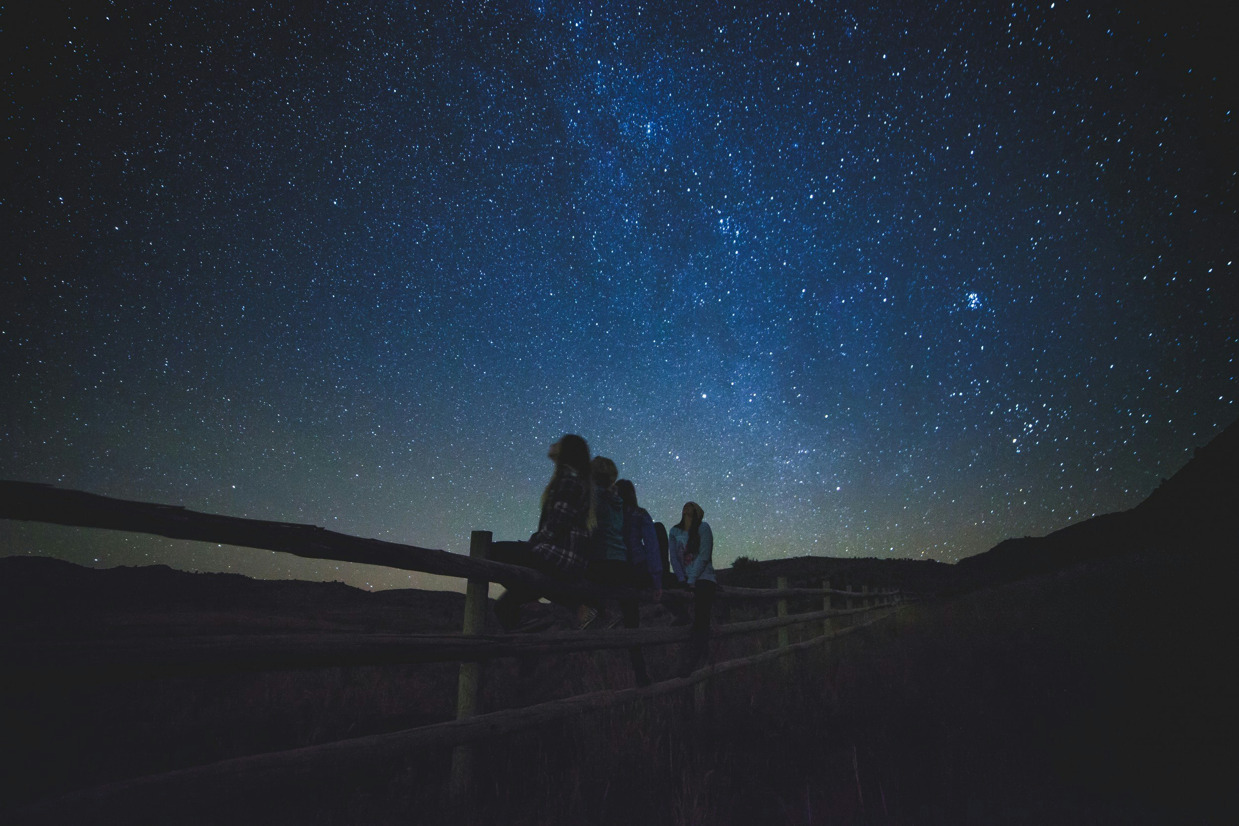 several women sitting on fence watching milky way